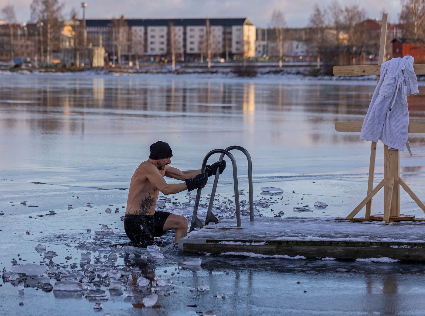 A man getting into a hole cut in a frozen lake outdoors, holding onto a ladder.