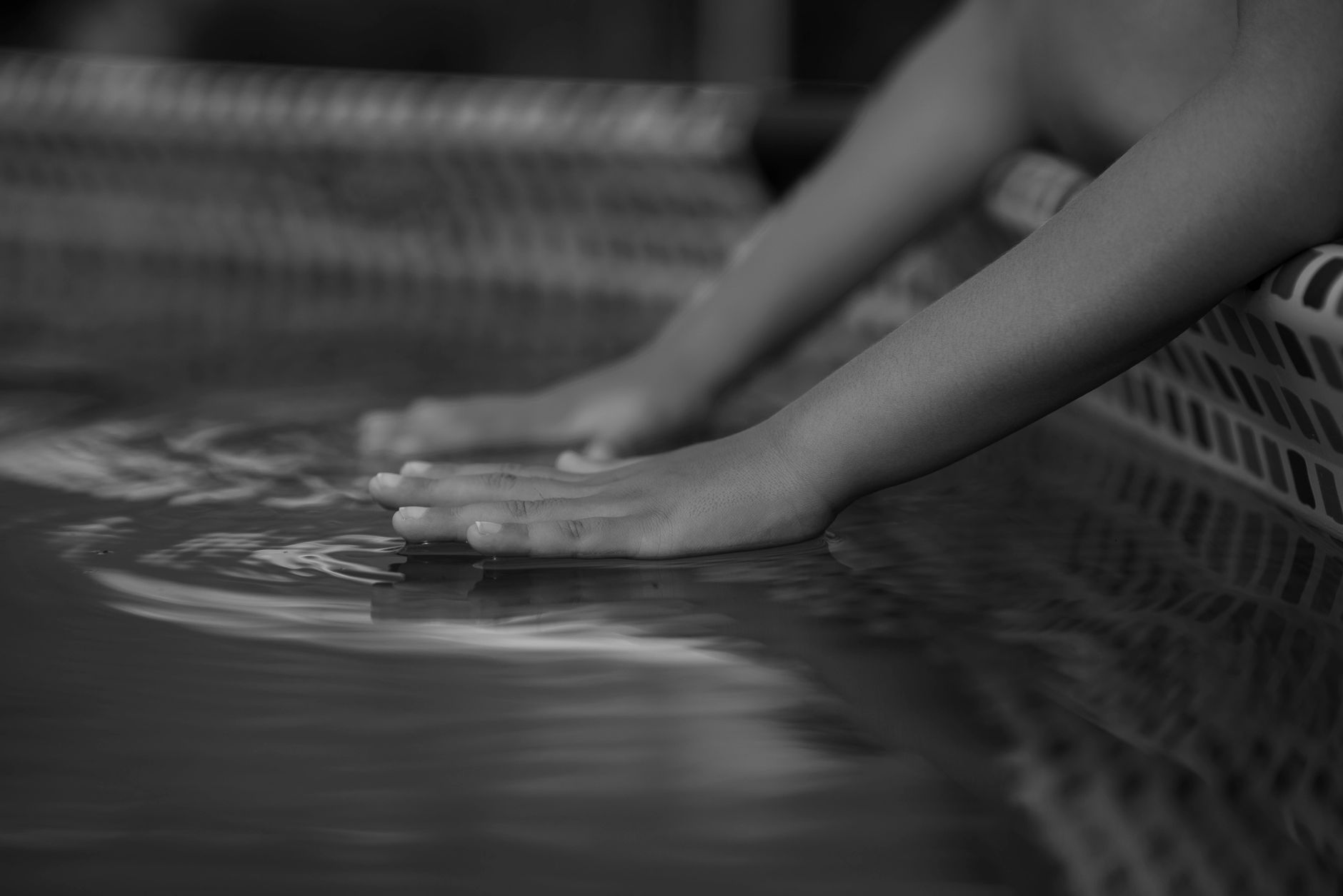 A black and white photo of a person's hands and arms resting on the surface of the water in a tub or pool.